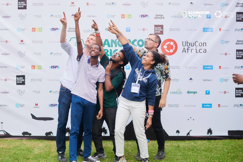Five members of Djangonaut Space meeting up at DjangoCon Africa 2025, pointing to the sky!