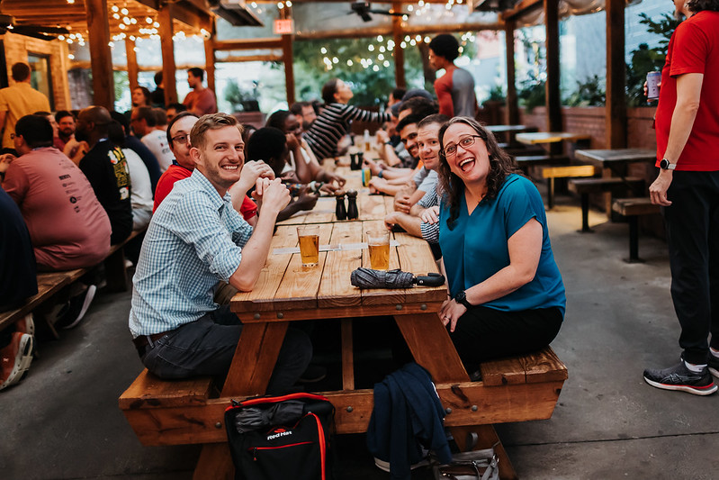 A photo of myself and Rachell sitting at a bench amidst the DjangoCon US crowd. I'm laughing too hard and Rachell is smiling broadly.