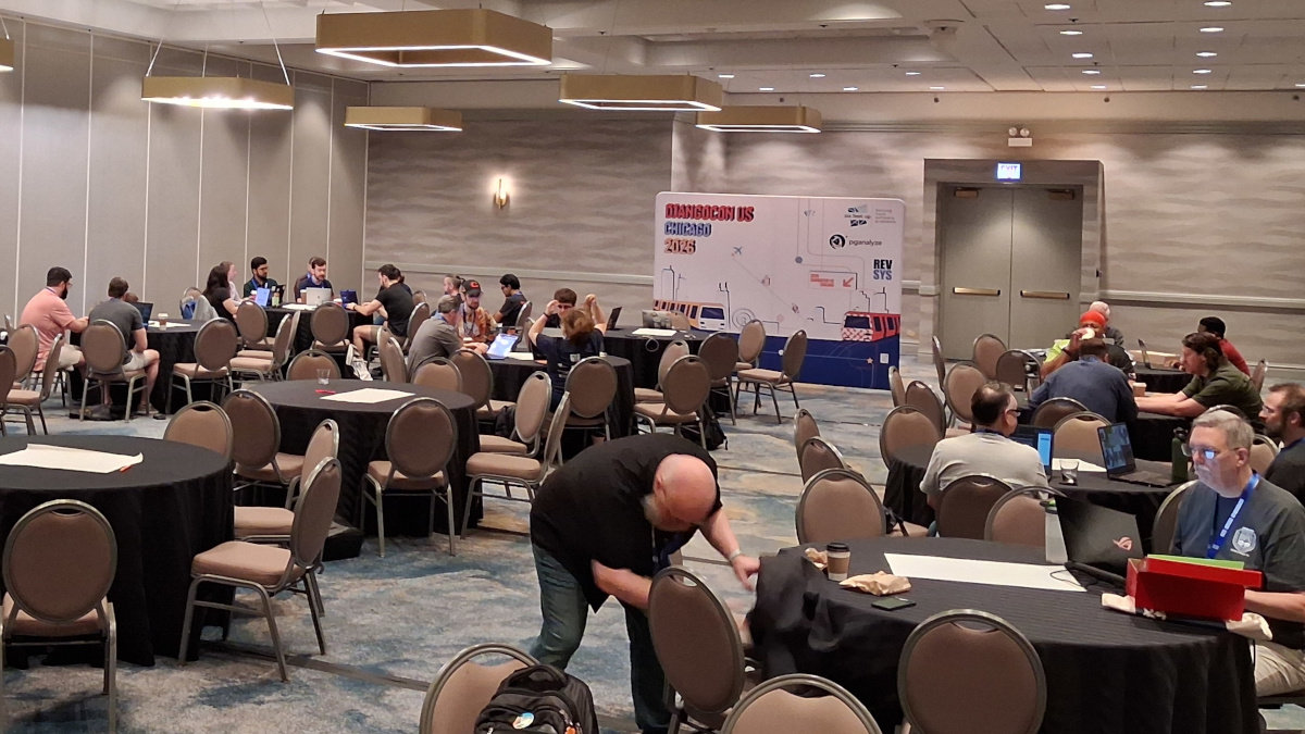 A partial view of the sprints area at DjangoCon US. There are tables of people collaborating with the big DjangoCon US 2026 sign in the background.